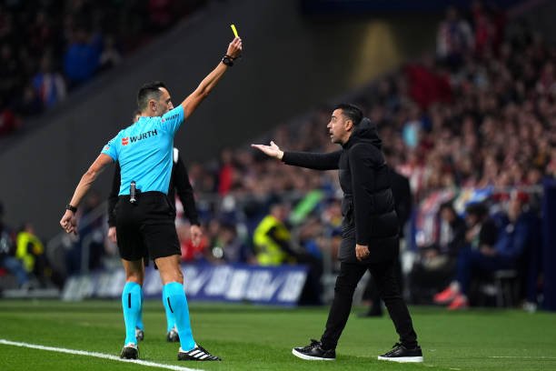 MADRID, SPAIN - MARCH 17: Match Referee Jose Maria Sanchez Martinez shows Xavi, Head Coach of FC Barcelona, a yellow card during the LaLiga EA Sports match between Atletico Madrid and FC Barcelona at Civitas Metropolitano Stadium on March 17, 2024 in Madrid, Spain. (Photo by Angel Martinez/Getty Images)