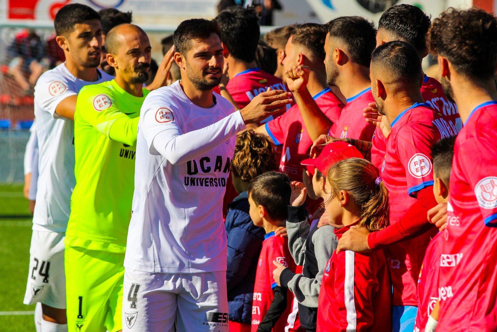 Imagen del momento en el que los jugadores de la Deportiva Minera y el UCAM se daban la mano antes del partido. Fuente: UCAM Murcia "X"