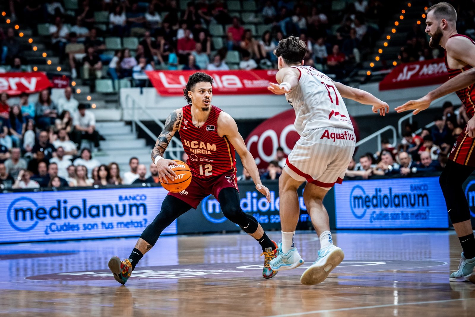 Jonah Radebaugh piensa a quién pasarle el balón con Saint Supery encima. Fuente: UCAM Murcia "X"